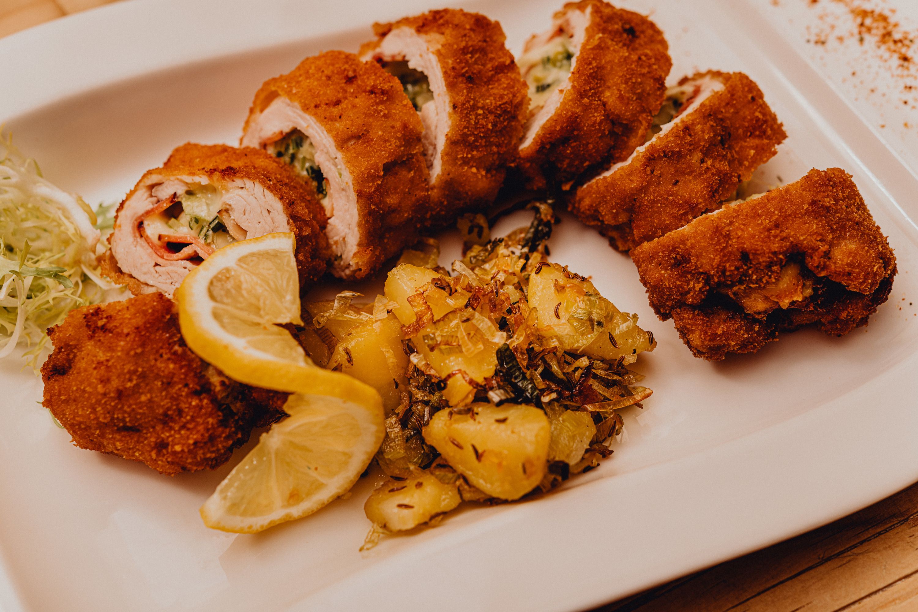 Stuffed baked turkey fillet with potato garnish and lemon slices on a white plate.