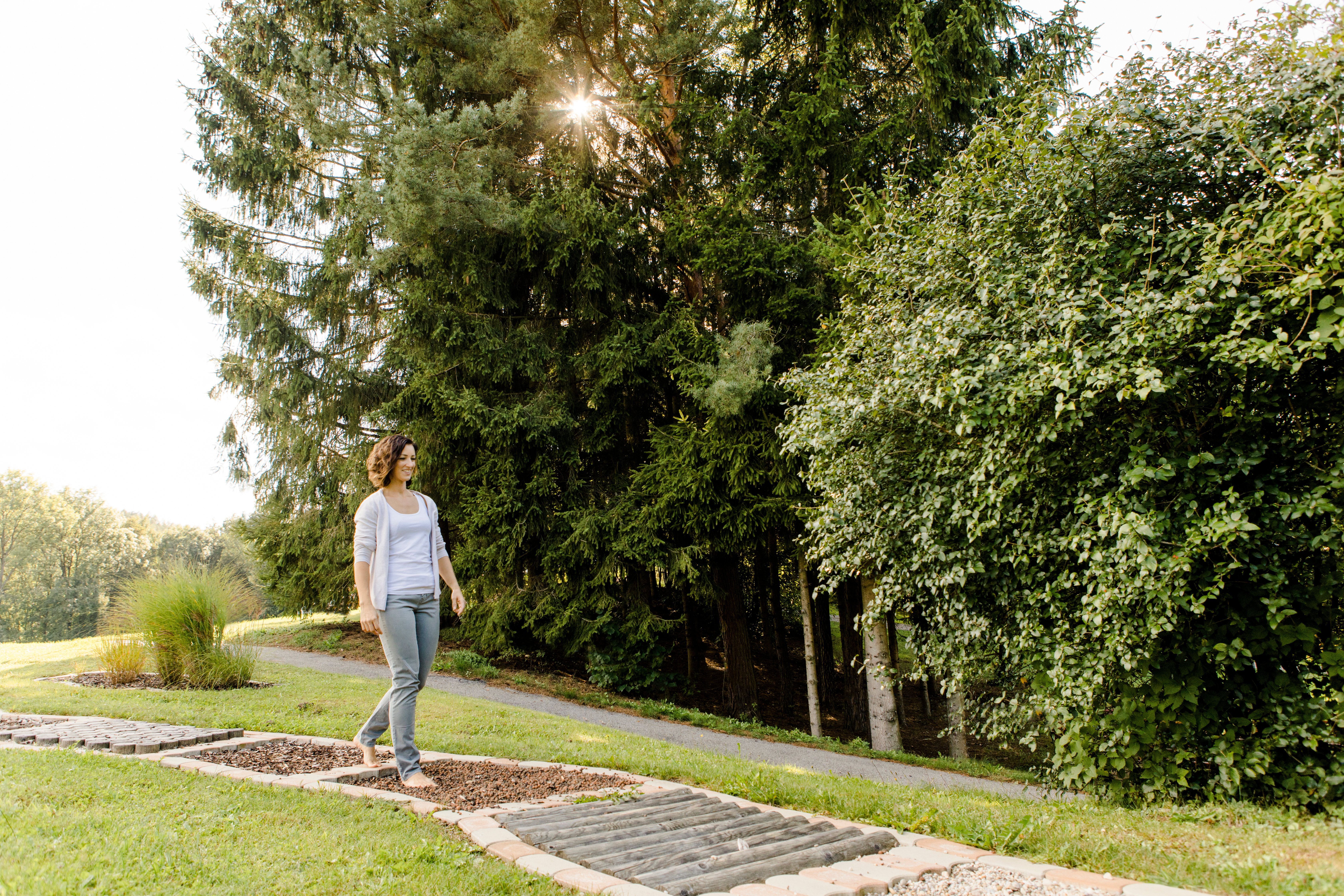 A woman walks barefoot on a path in the spa gardens of Bad Schönau, surrounded by trees and grass.