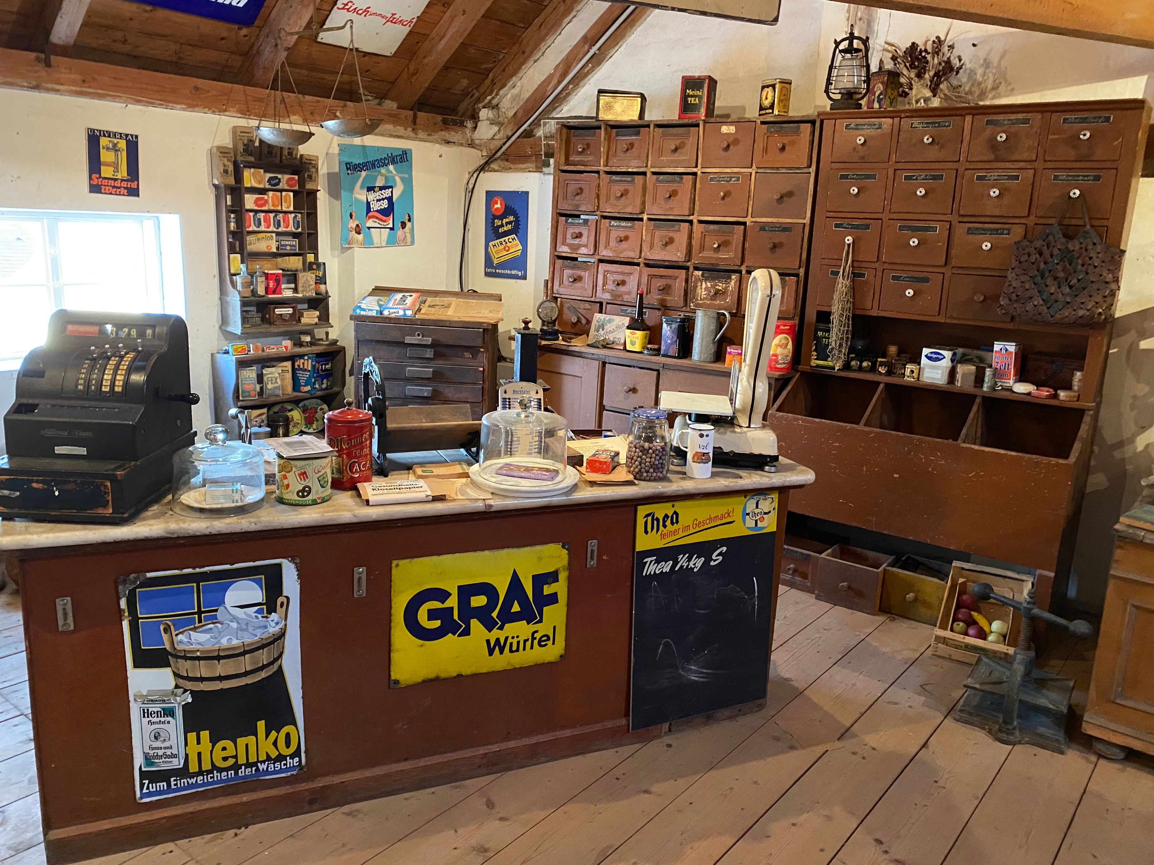 Interior view of a historic corner store with an old cash register, scales and shelves full of goods.