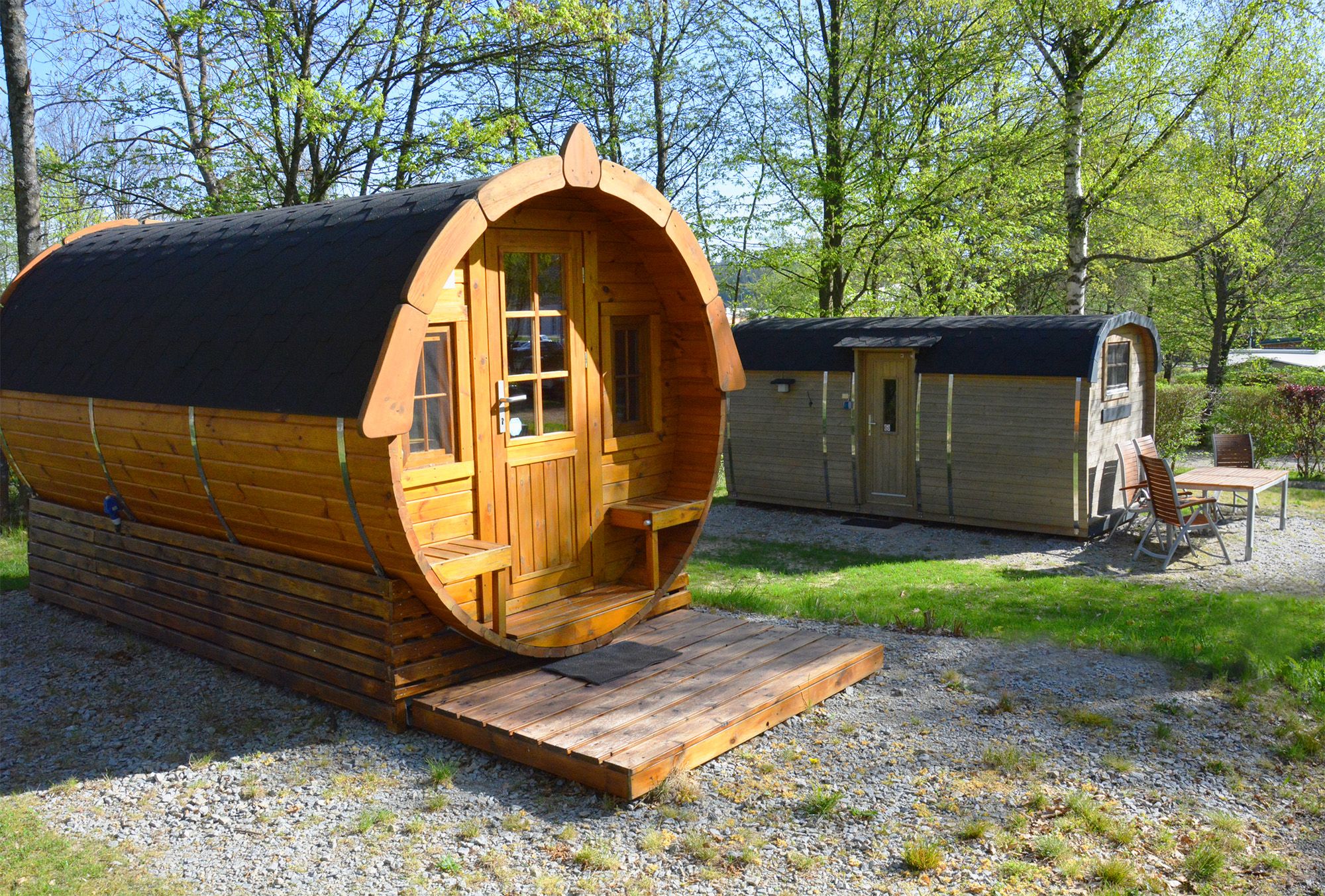 Two wooden barrel huts in a green park with trees.