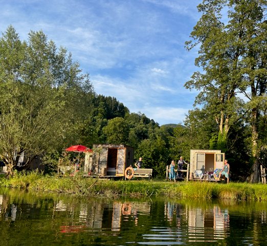 A sleeping pod with a red parasol on the shore of Neubrucker Pond, surrounded by trees.