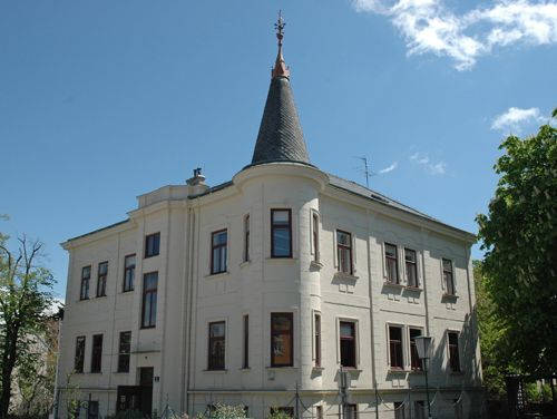 Historic building with tower and many windows, surrounded by trees.