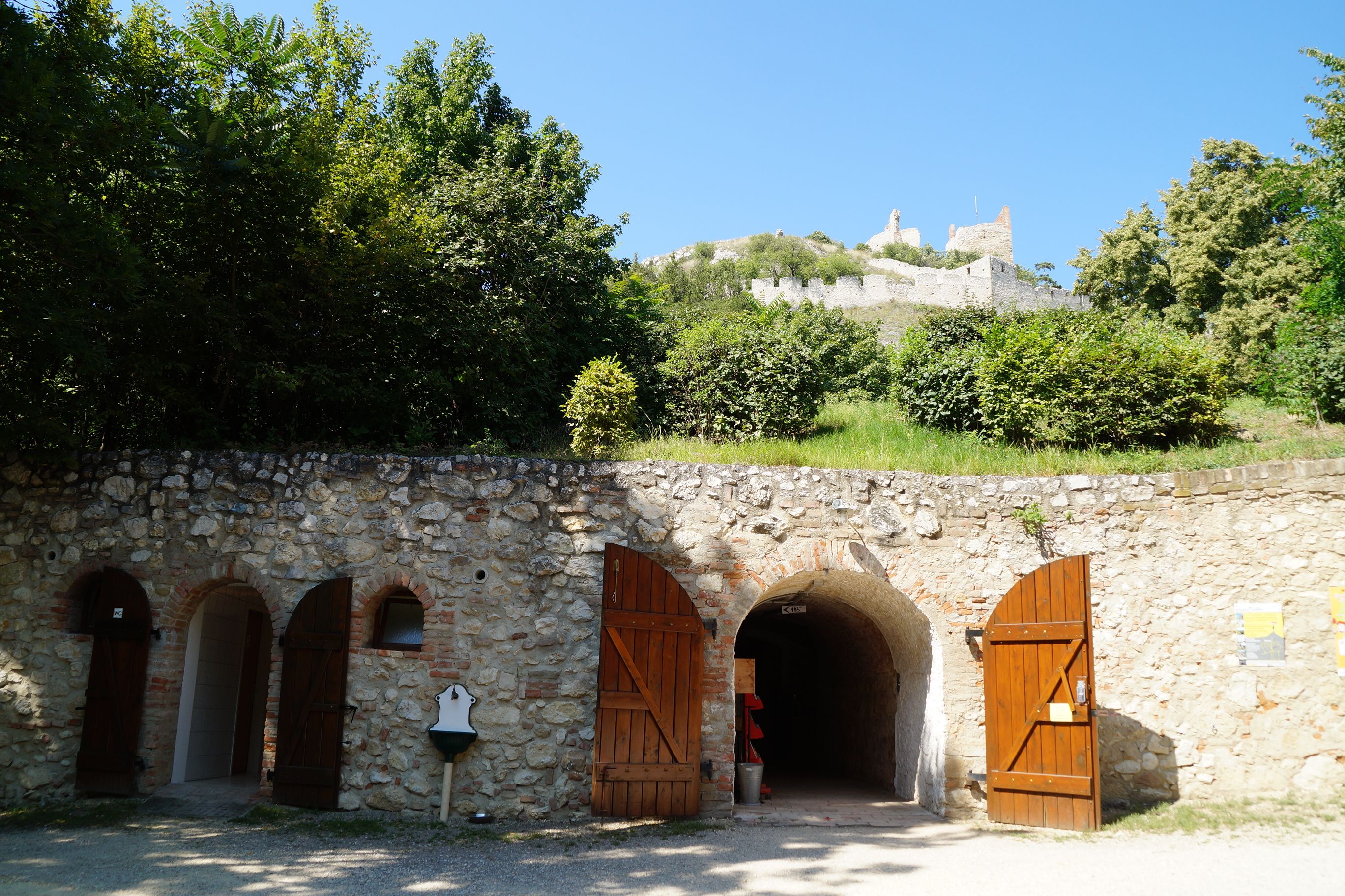 Entrance to a castle cellar with wooden doors, above a ruined castle on a hill.