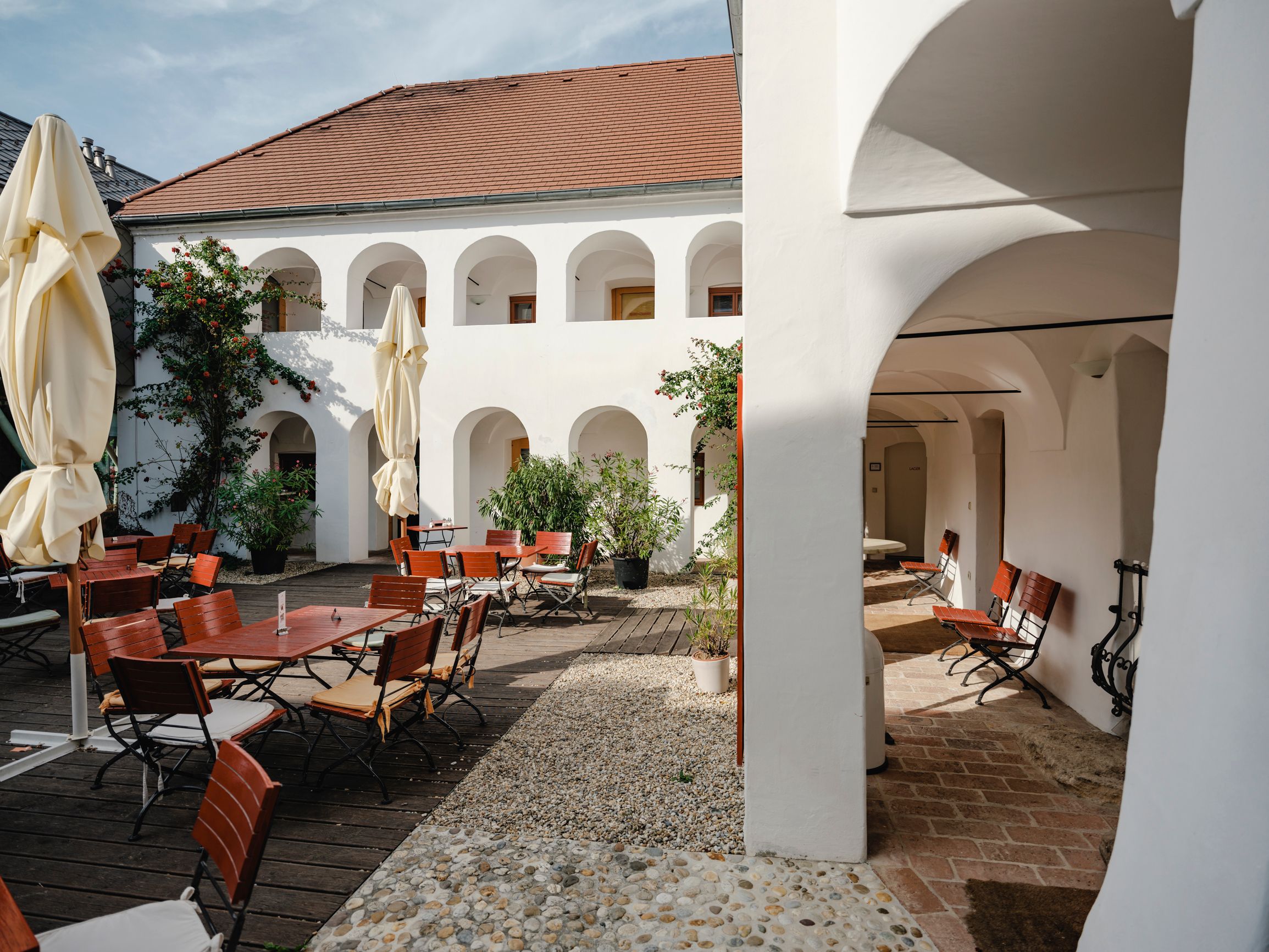 Inner courtyard with white arcades, wooden furniture and parasols.