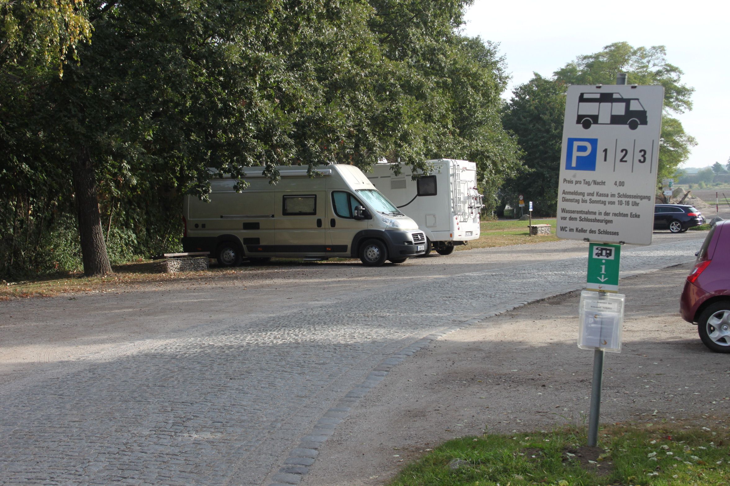 Motorhome parking area with two parked motorhomes and a sign.