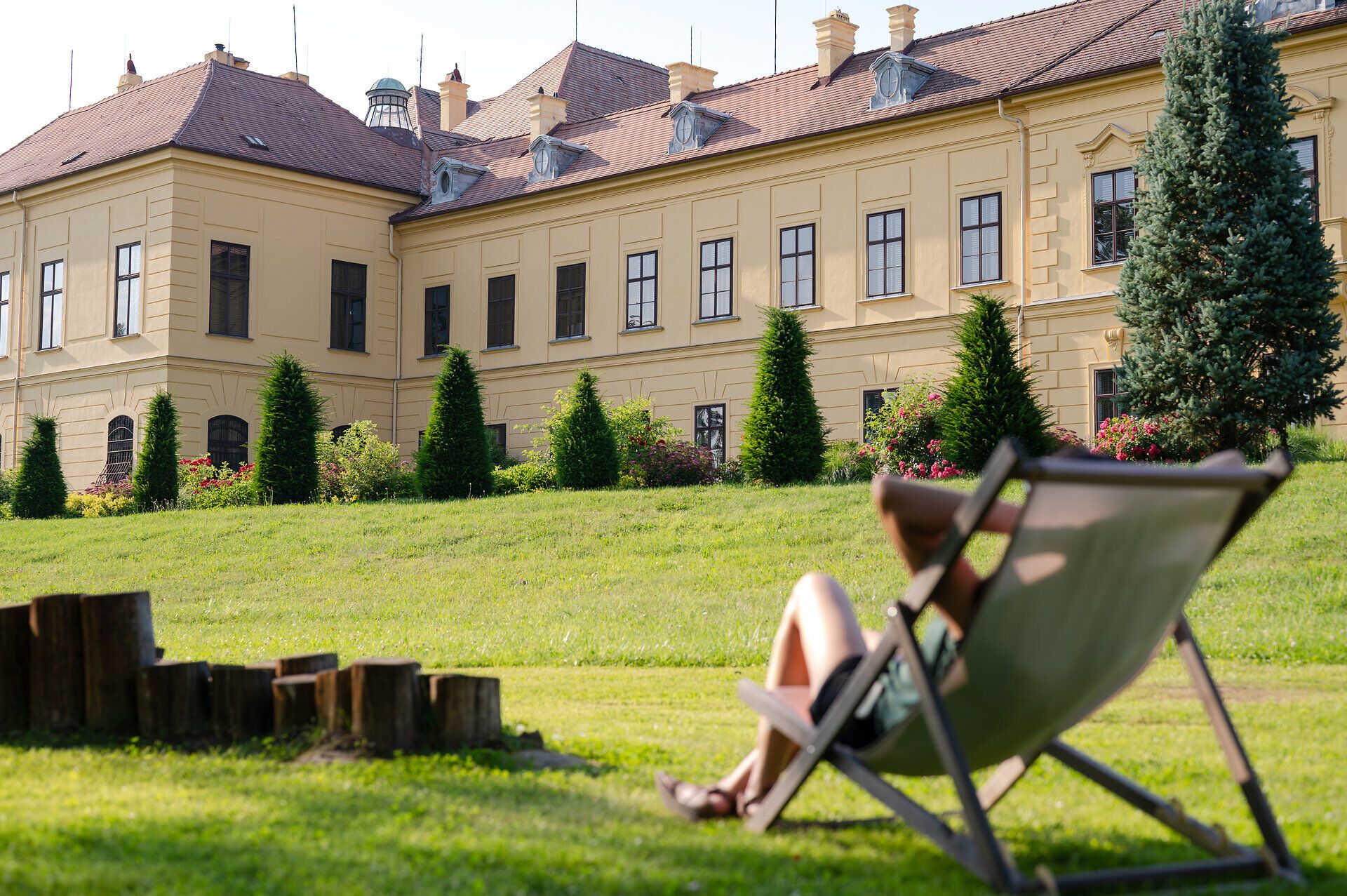 Woman in a deck chair on a green meadow looking towards Eckartsau Castle. 