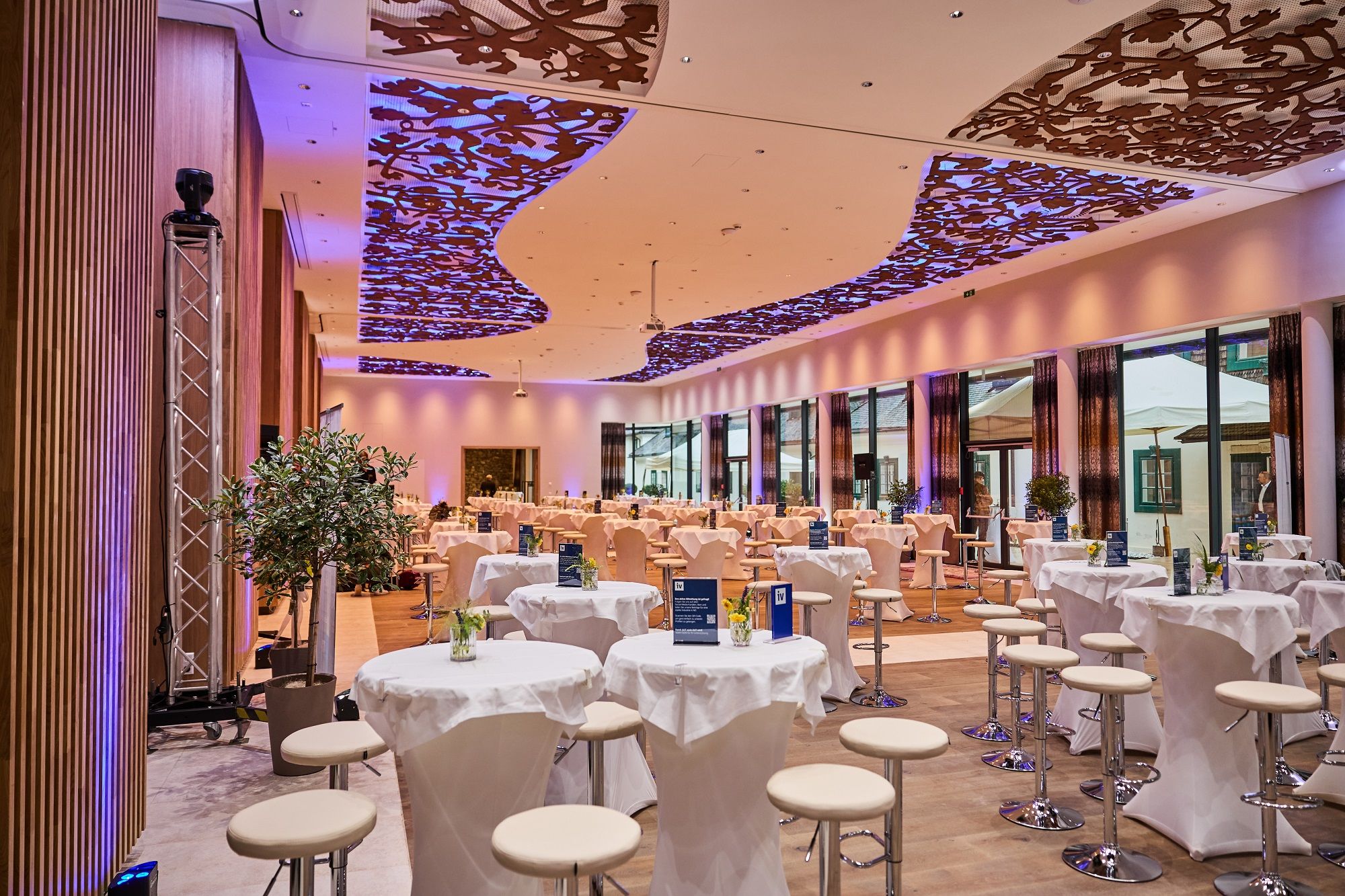 Interior view of a modern event hall with decorative ceiling and round tables.