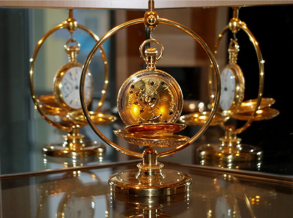 Golden pocket watch in a decorative stand, reflected in a mirror.