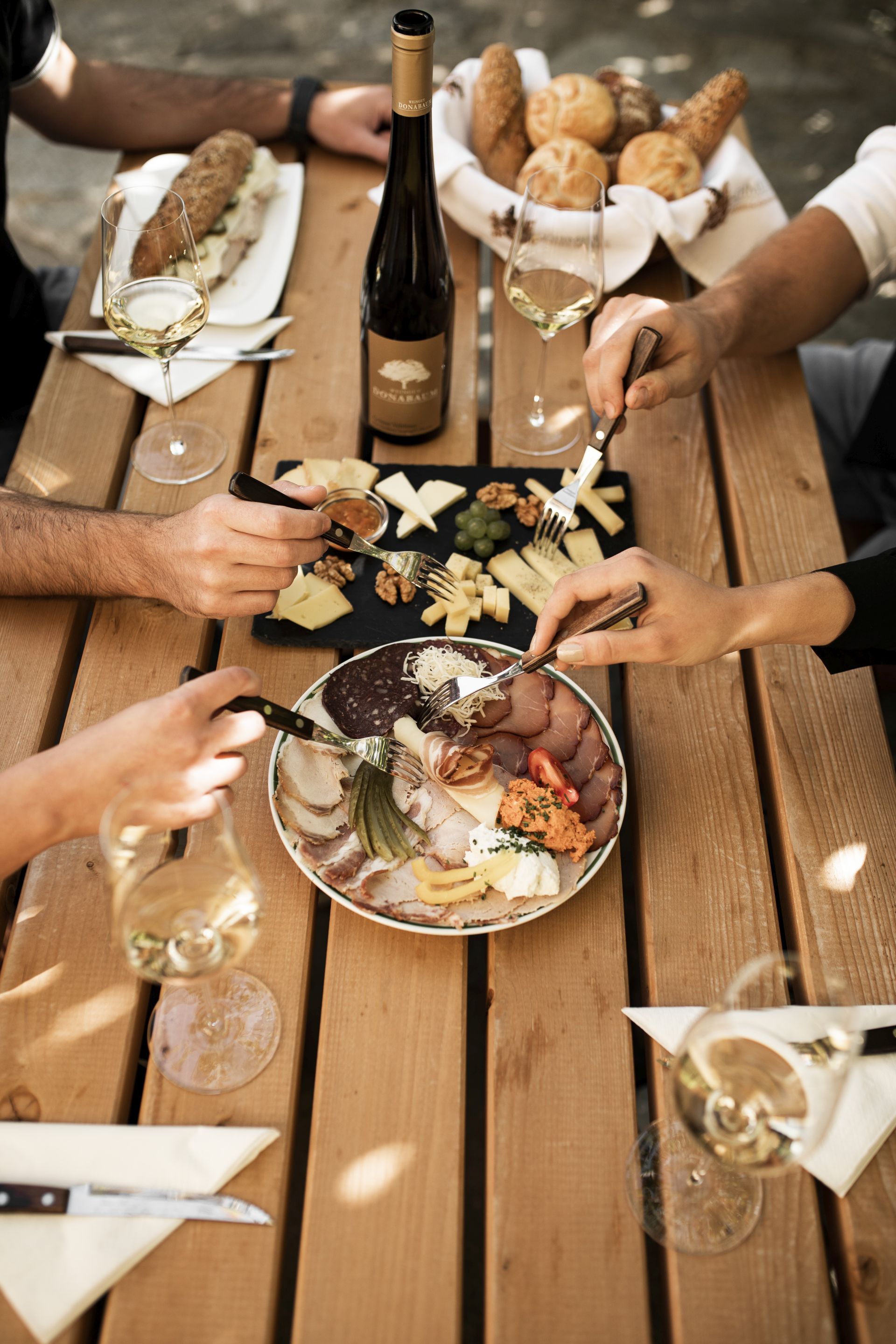 A table with a bottle of wine, glasses, cheese platter and cold cuts.
