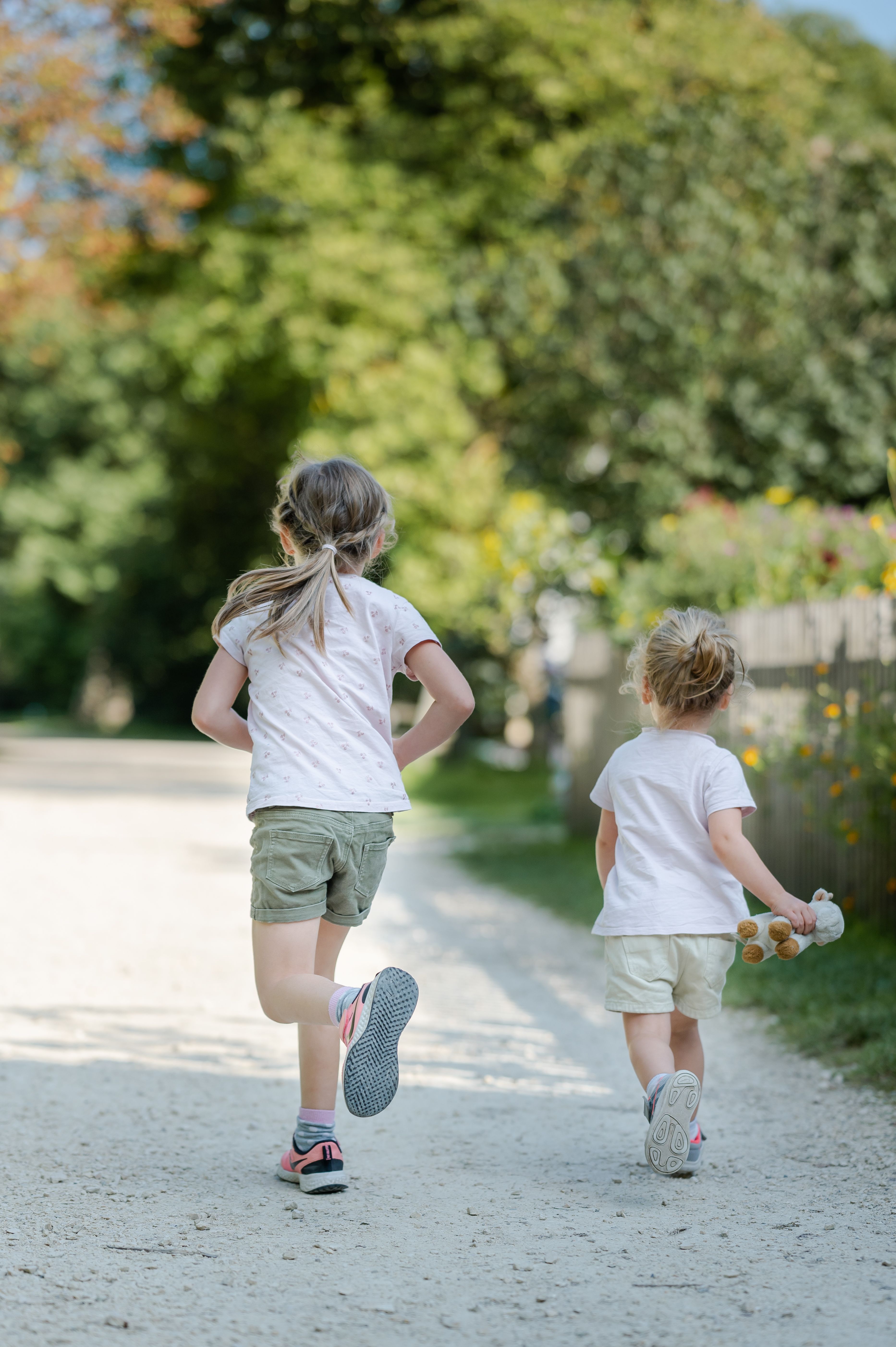 Two children running on a gravel path in a green park.