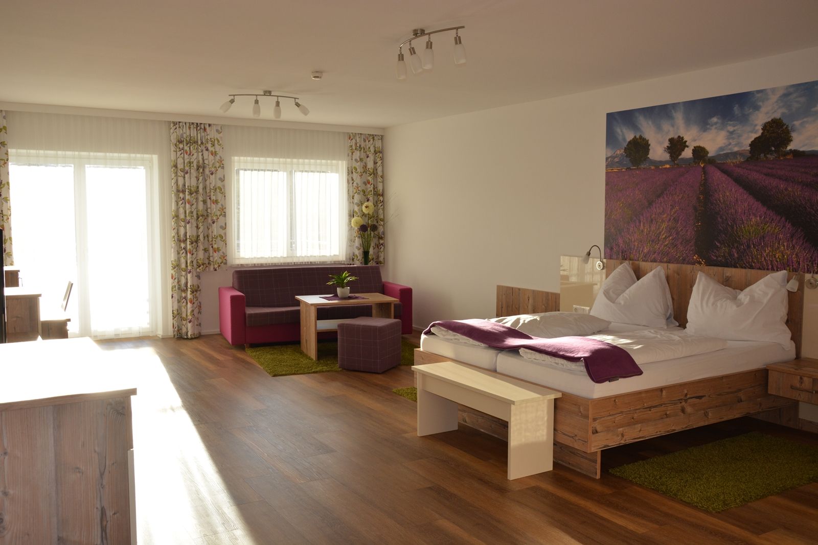 A modern double room with a wooden floor, a large bed, a sitting area and a picture of lavender fields on the wall.