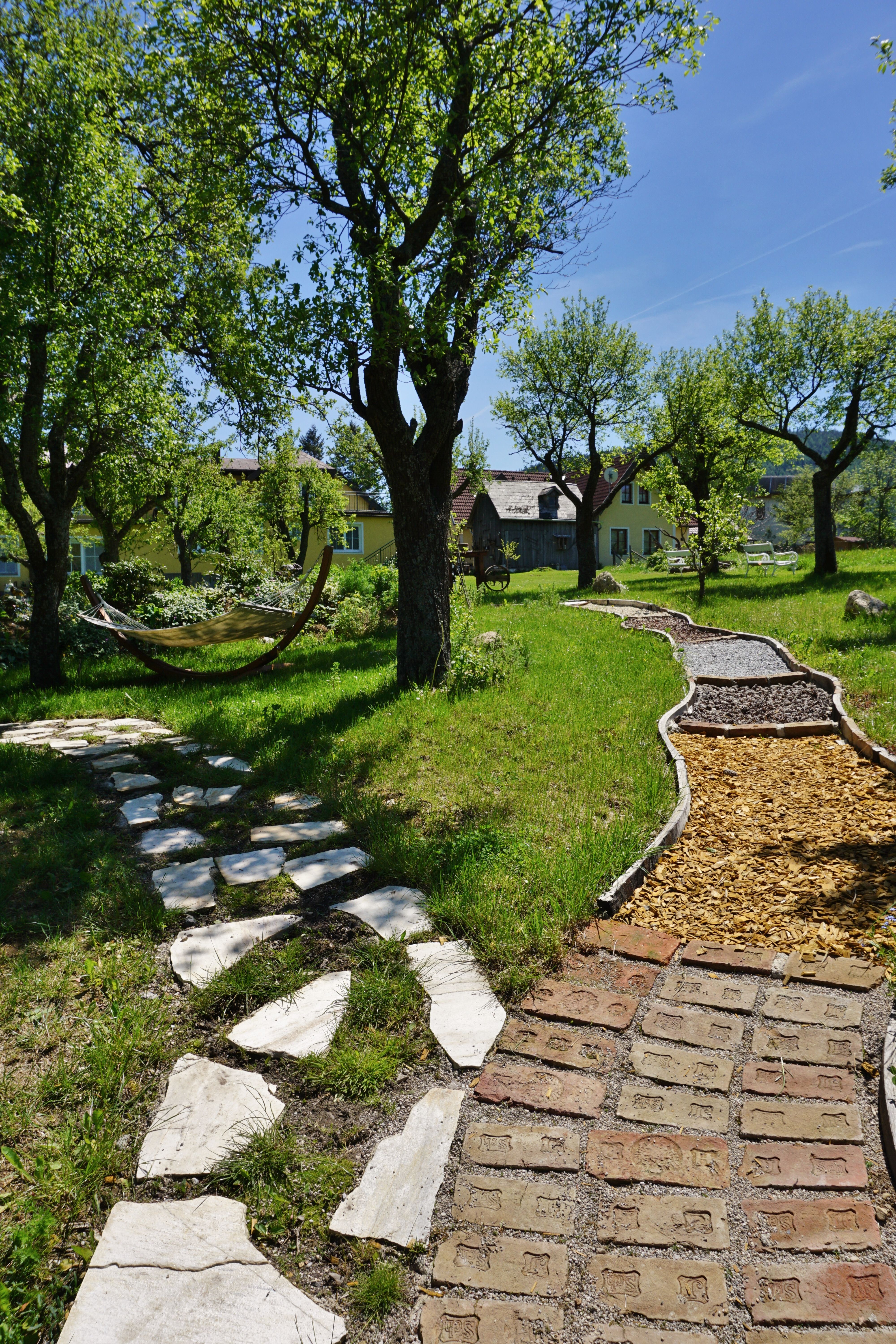 A barefoot path with different materials in a green garden with trees and a hammock.