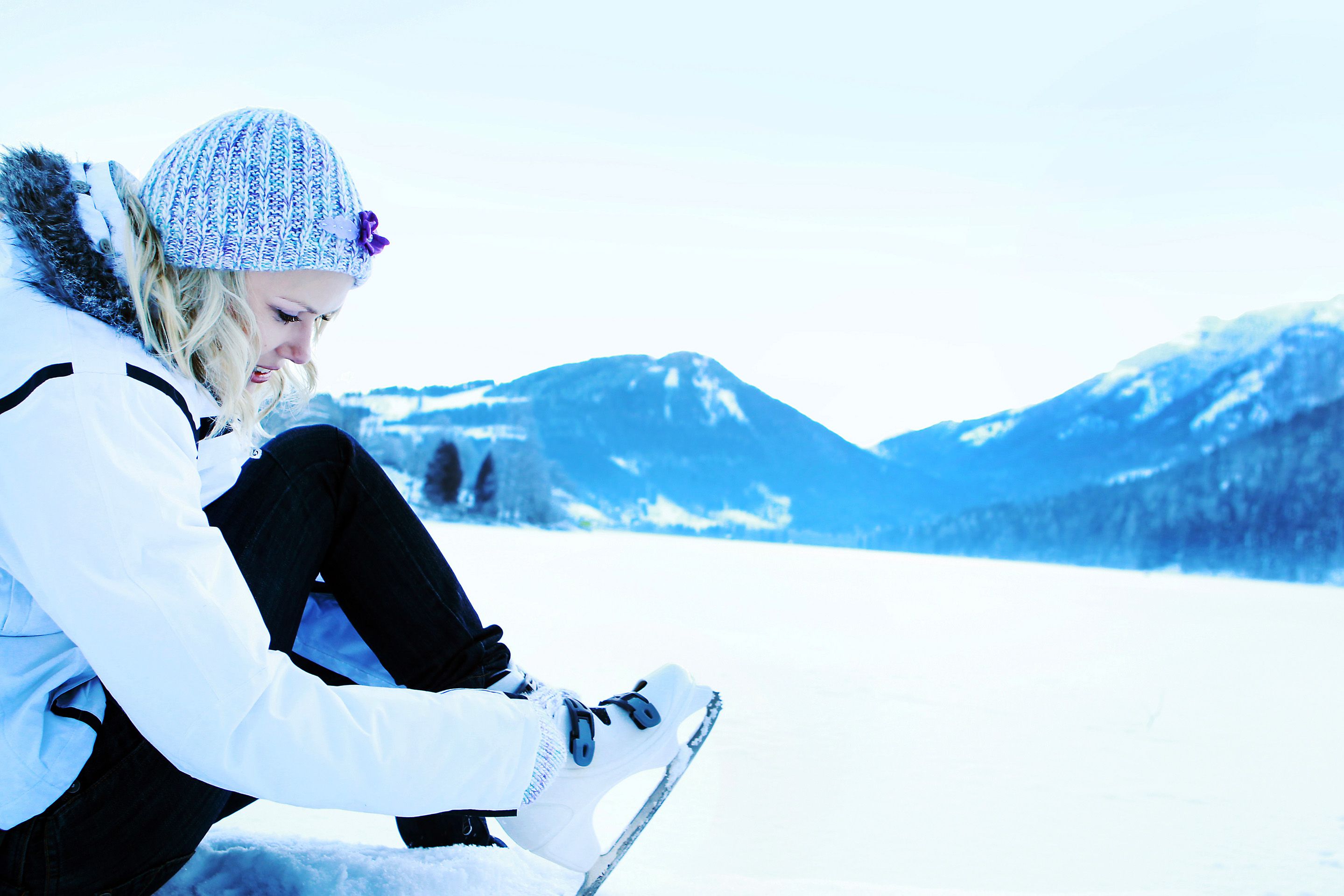 Person puts on ice skates on a snowy lake surrounded by mountains.