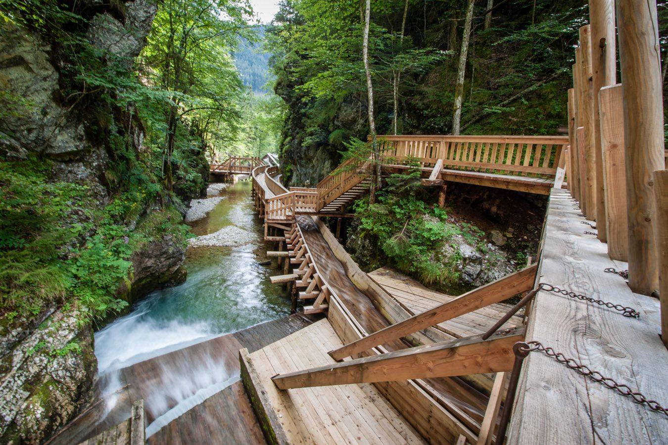 Wooden footbridges in the Mendlingtal valley along a stream in a wooded gorge.