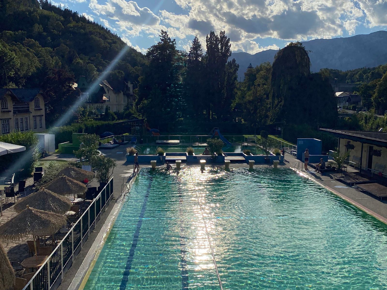 An outdoor pool with clear water, surrounded by trees and mountains in the background.