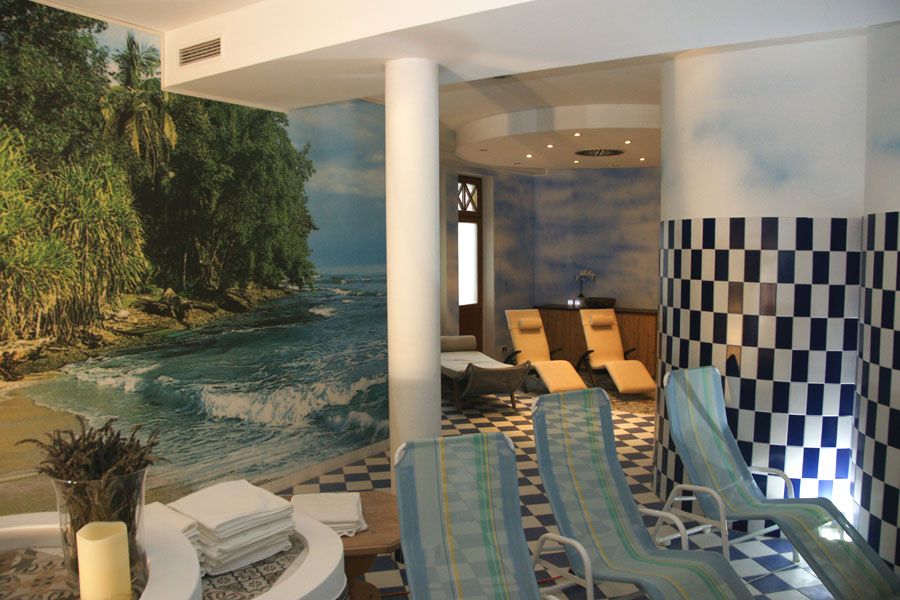 A sauna area with sun loungers, a mural of a beach and blue and white checkered tiles.
