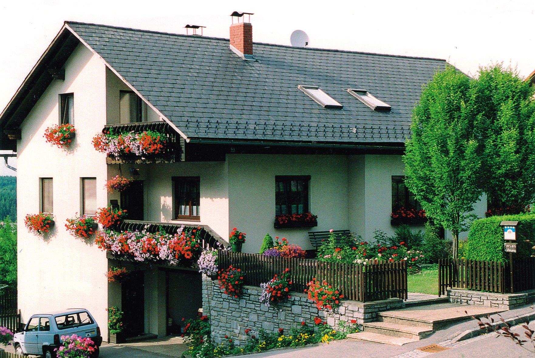 A two-storey house with balconies decorated with flowers and a small garden.