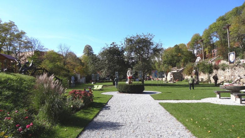 A well-tended garden with sculptures and walkers in sunny weather.