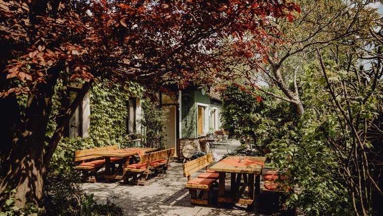 Cozy beer garden with wooden benches, surrounded by lush greenery and trees.