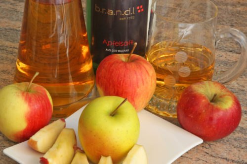 Different types of apples and apple juice on a table.