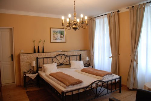 A cozy bedroom with a double bed, chandelier and large windows with curtains.