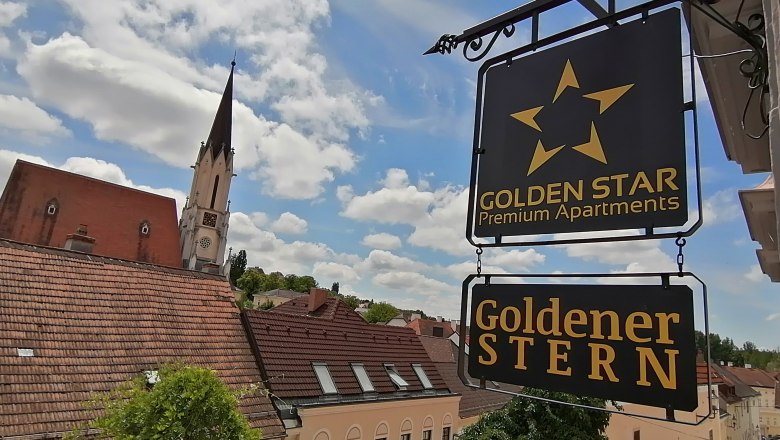 Exterior view, © Inhaber Peter Mayer View of a sign with the inscription 'Golden Star Premium Apartments' and 'Golden Star' in front of a church tower and rooftops.