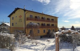 Yellow building called Sonnenhof covered with snow in winter, blue sky in the background.