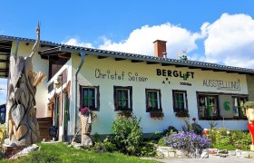 A building with the inscription 'Bergluft' and wooden sculptures in the foreground.