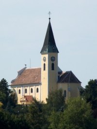 Großebersdorf parish church with pointed tower and clock, surrounded by trees.