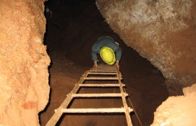Person wearing a helmet climbs down a ladder in a cave.
