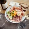 A plate of cold cuts, vegetables and bread, surrounded by wine glasses and a bottle of wine on a table.
