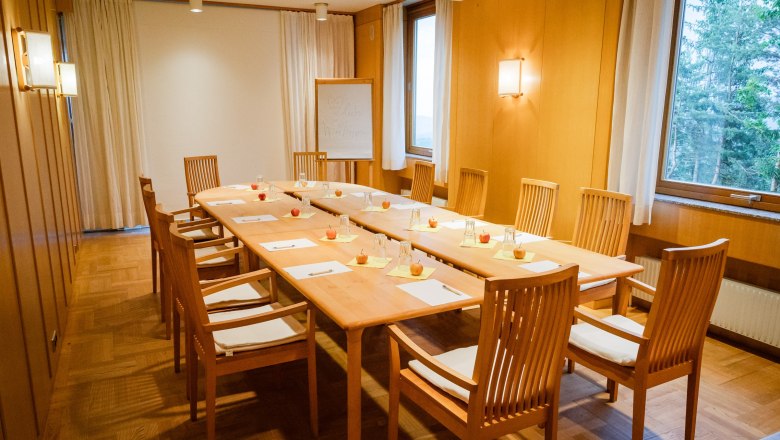 A seminar room with a long wooden table surrounded by chairs. There are notepads, pens and apples on the table.