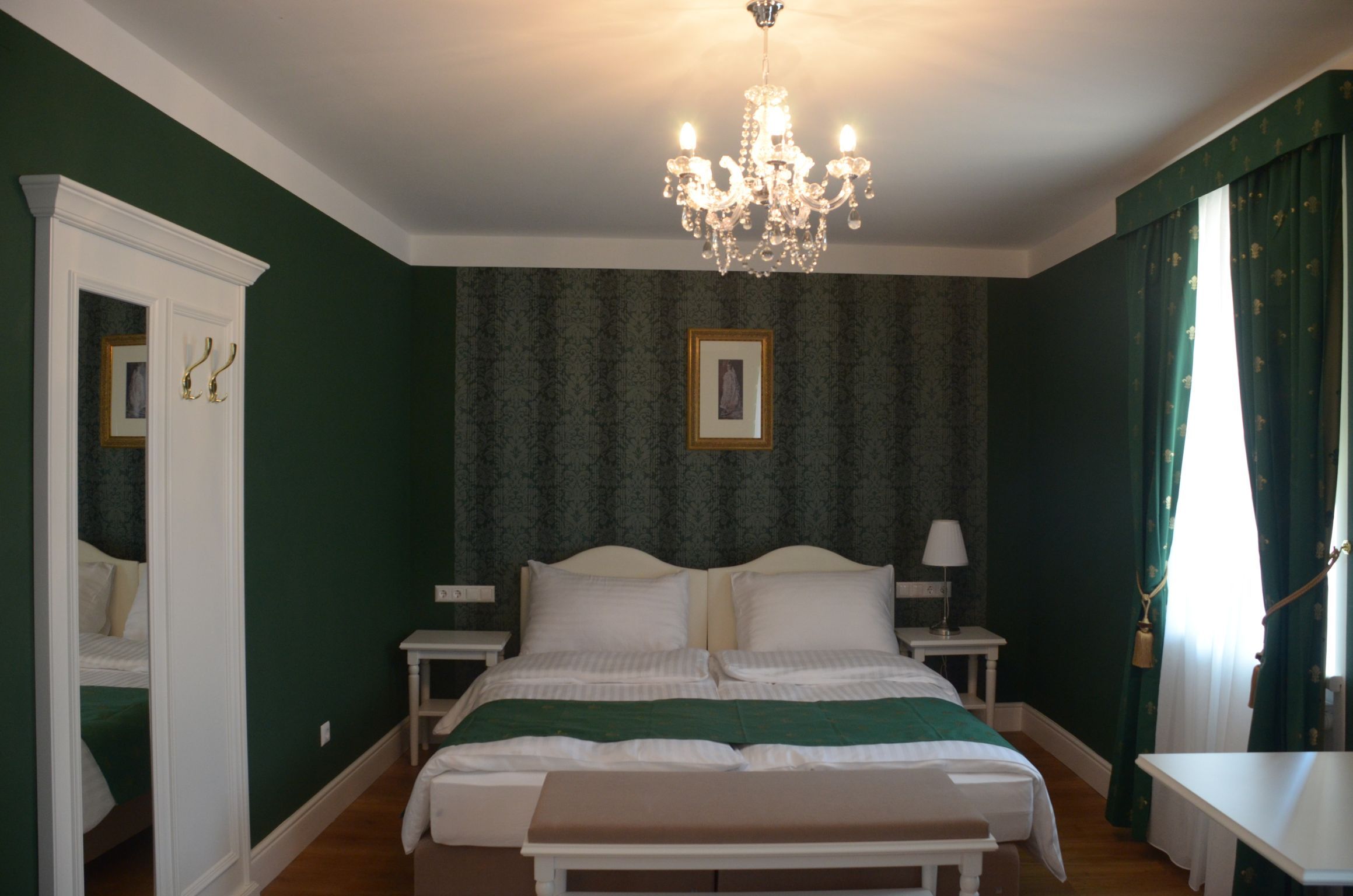 Elegant hotel room with green decor, double bed, chandelier and curtains.