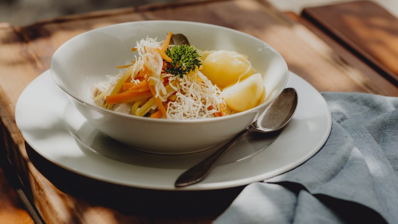 A plate of horseradish meat, root strips and salted potatoes, garnished with parsley, on a wooden table.