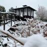 Snow-covered Zen garden with wooden bridge and pavilion in the background.