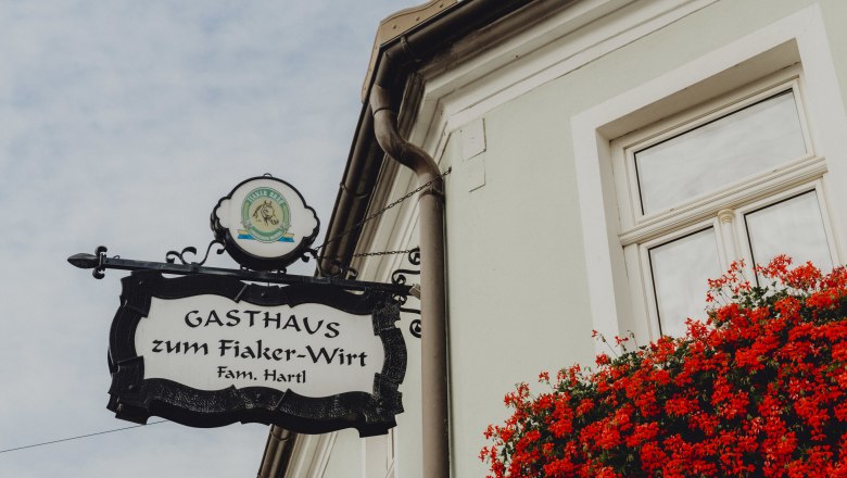 Sign for the Fiaker-Wirt inn in Langenlois with red flowers in the window.