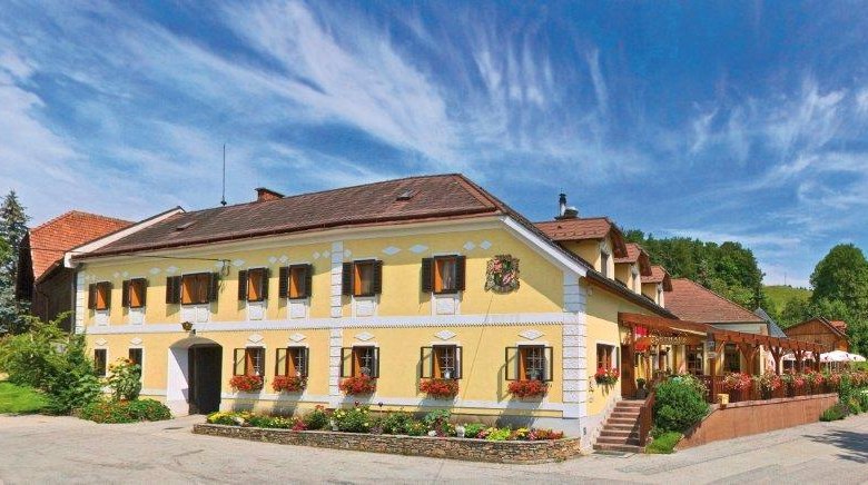 Gasthof Buchegger, © Gasthaus Buchegger, Foto Mayrhofer A. Z. Traditional inn with yellow façade, surrounded by green landscape and blue sky.