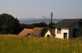 Rural scene with houses and meadows in the foreground, hills in the background.