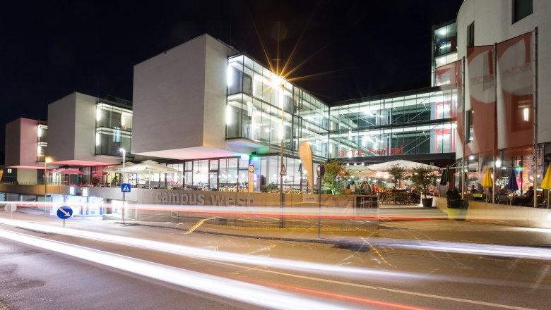 Night shot of a modern building complex with glass fa&ccedil;ade and illuminated interiors.