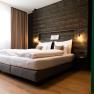 Modern hotel room with large bed, wooden wall and hanging lamps.