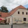 A yellow building with a red tiled roof and the word 'SOLA' on the wall. There are parasols and tables in front of the building.