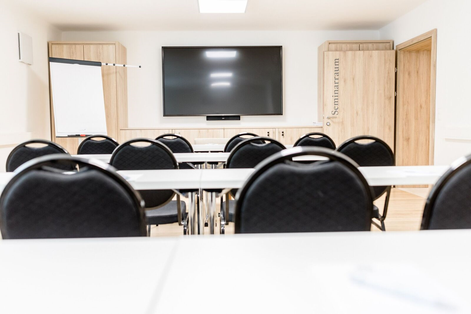 A modern seminar room with chairs, tables, a large screen and a flipchart.