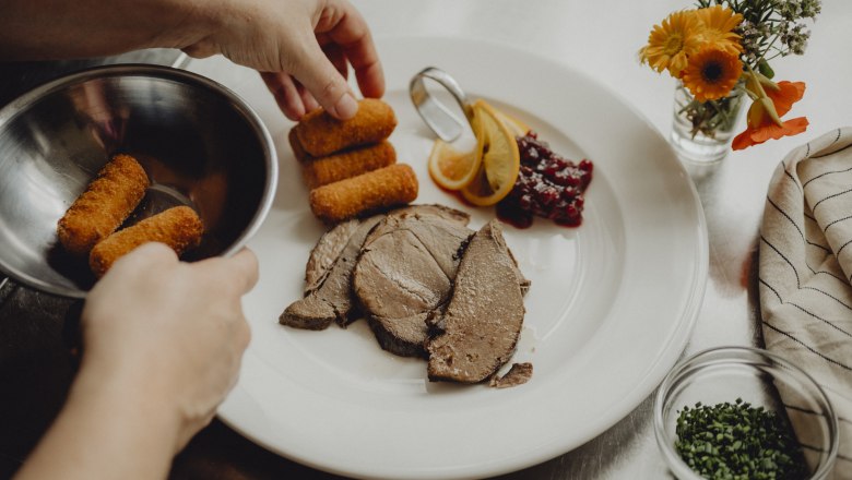 A plate with meat, croquettes, cranberries and lemon slices is served.