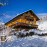 A wooden house in the snow with a blue sky in the background.