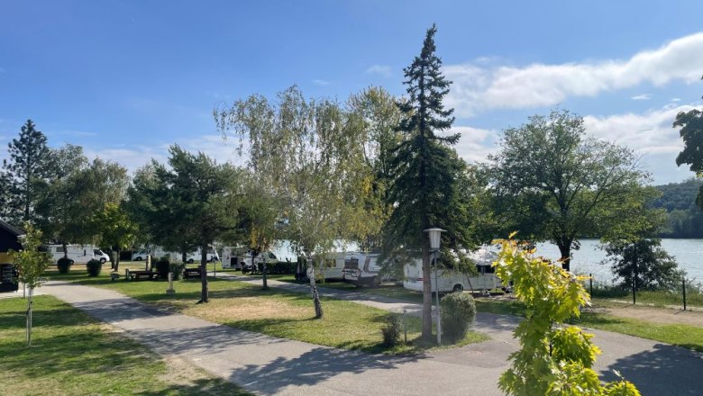 Campsite with mobile homes and trees on the lakeshore in sunny weather.