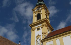 Yellow steeple of the Stockerau parish church against a blue sky.