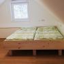 An attic room with a wooden double bed and green bed linen, with a white chest of drawers next to it.