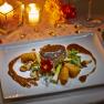 An elegant dish on a white plate, surrounded by candlelight and decorative elements.