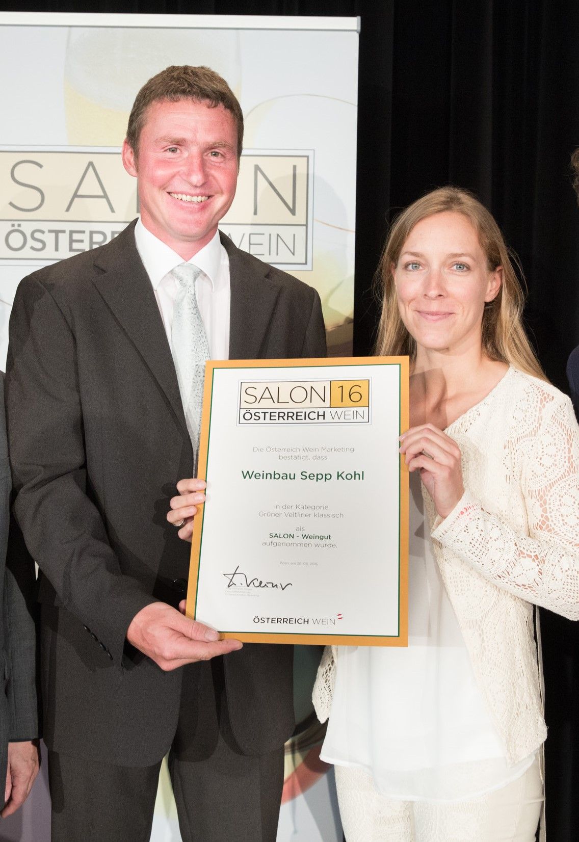 Two people holding a certificate with the inscription 'Weinbau Sepp Kohl' at an event.