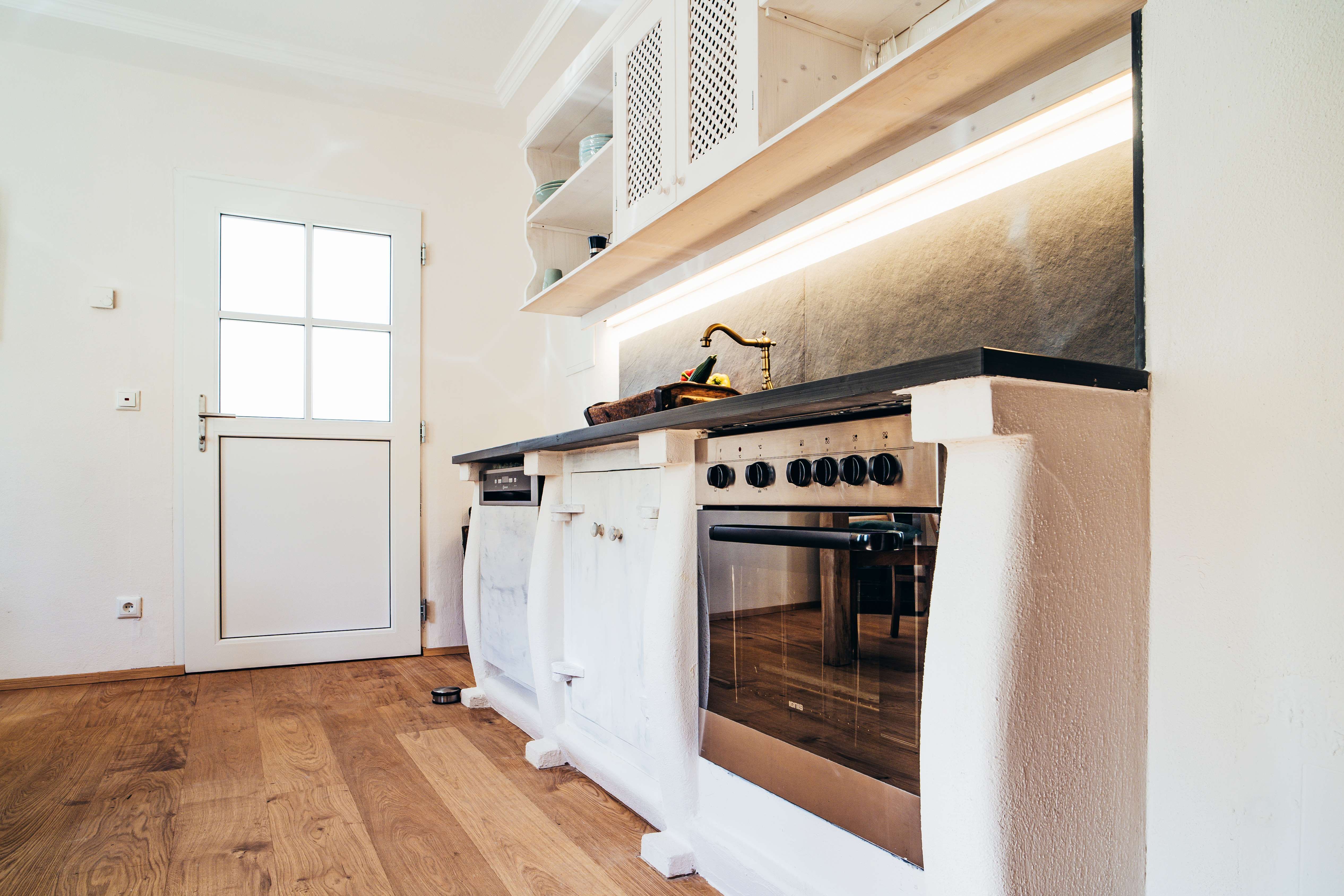 Modern kitchen with wooden floor, white door and stainless steel stove.